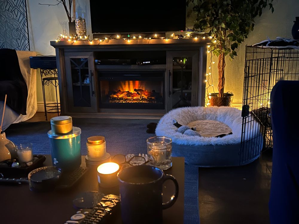 Fske fireplace on with a strand of white lights, coffee cup and candle in foreground 