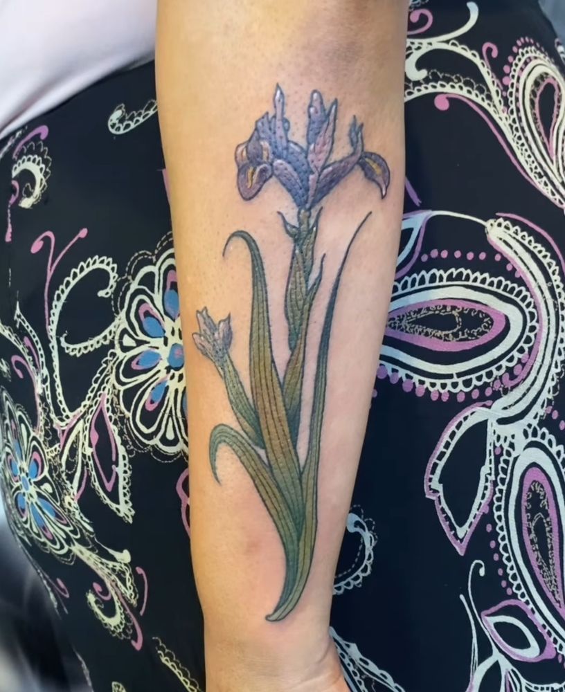 A color tattoo of a purple iris on the outer forearm 