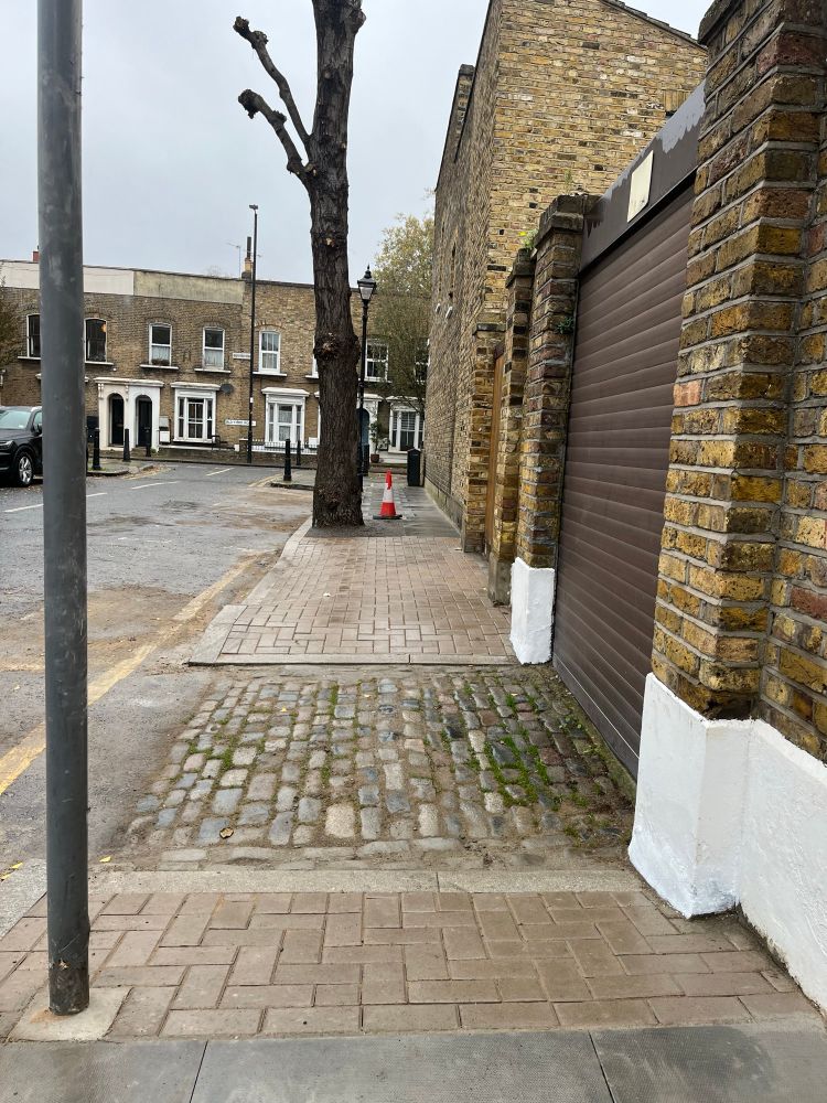 On the far side of an entrance way to a garage, the pavement has been relaid and now includes a dropped kerb