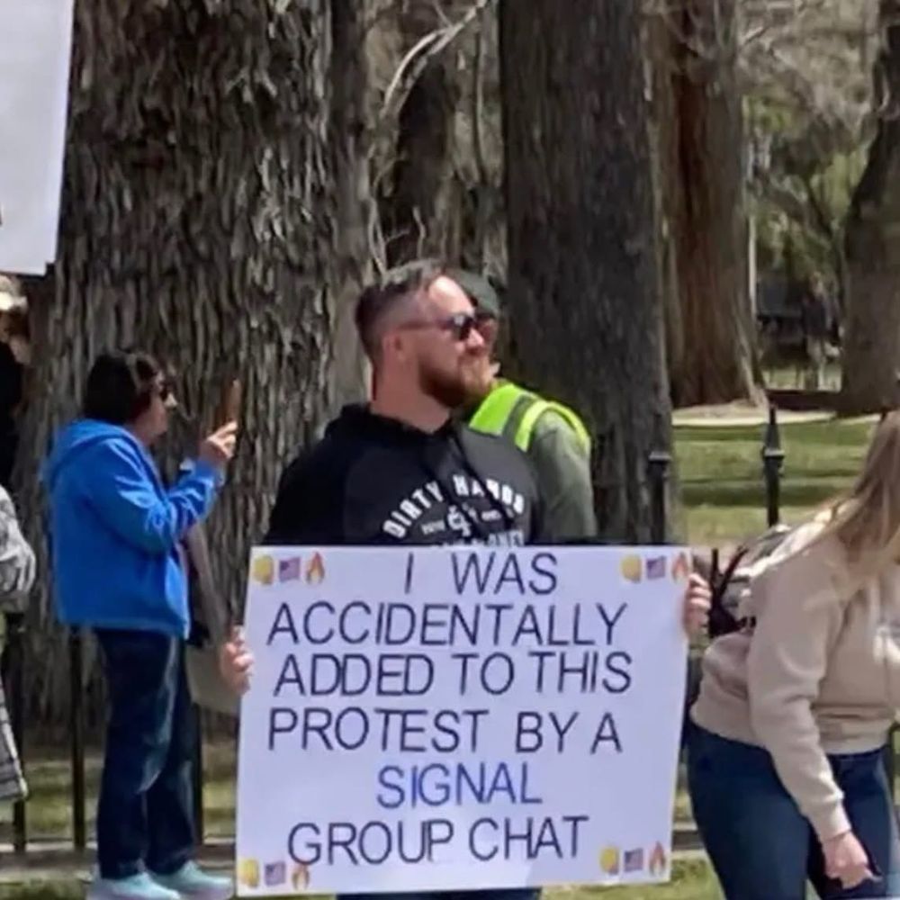 Man with a protest sign saying, “I WAS ACCIDENTALLY ADDED TO THIS PROTEST BY A SIGNAL GROUP CHAT.”