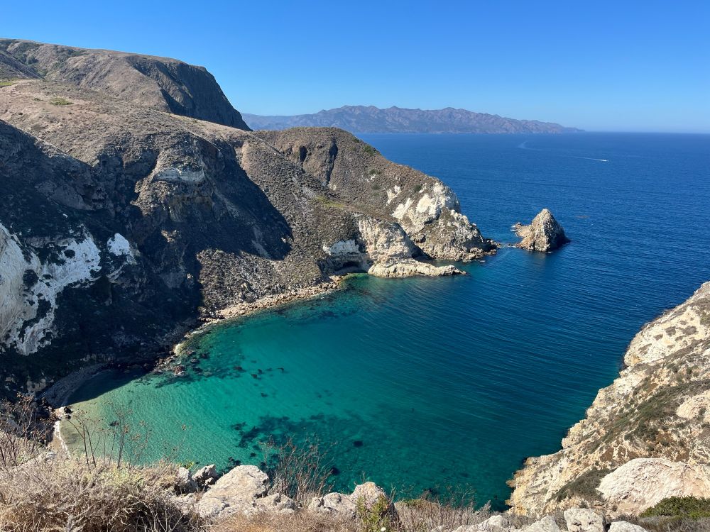 A sunny day at a a small blue green harbor surrounded by rocky cliffs.
