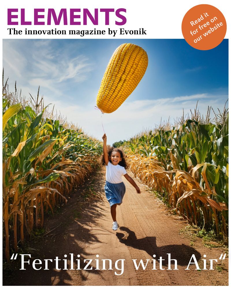 A AI-generated image shows a young girl running barefoot through a golden wheat field. In her hand, she holds the string of a giant balloon shaped like an ear of corn. The balloon gently floats above her, symbolizing the concept of using nitrogen from the air to support plant growth. Below the image, in clear, modern typography, it reads: "Fertilizing with Air."