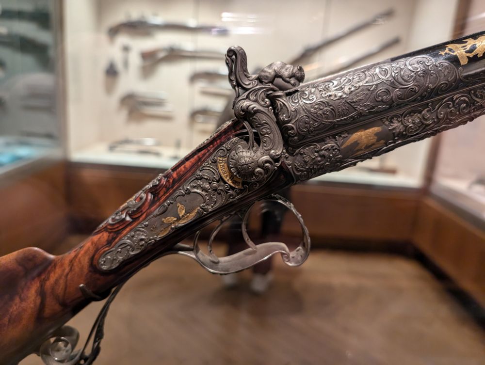 A closeup shot of an extremely ornate double barreled shotgun's firing mechanism and trigger. The hammers are shaped like squirrels holding nuts and there is floral filigree everywhere.