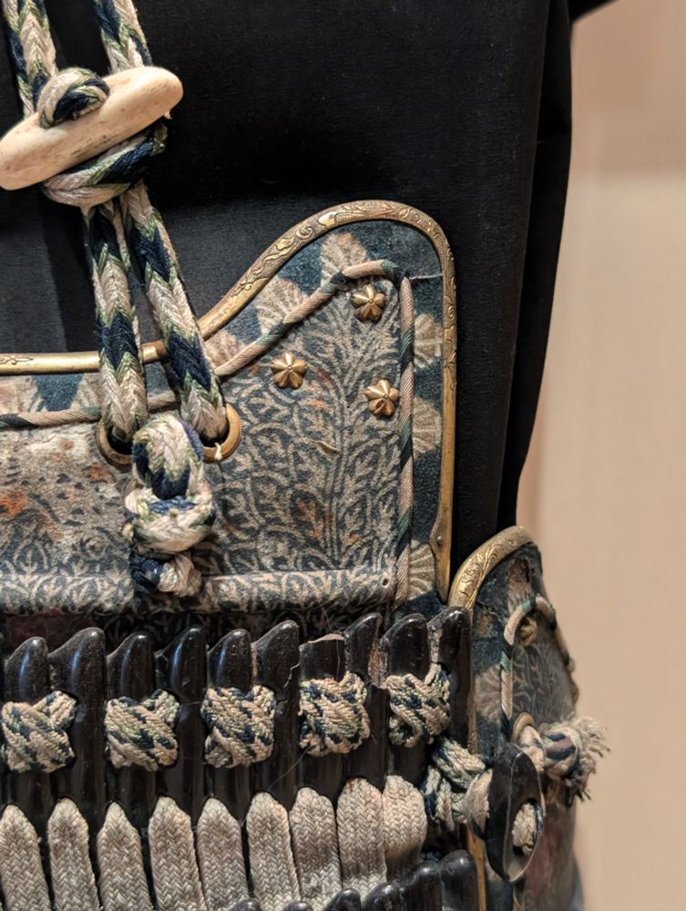 A closeup shot of some buttons, fasteners, and ties on a small section of a samurai armor set's front chest plate. There are various ornate patterns, complex knots, and overlapping pieces.