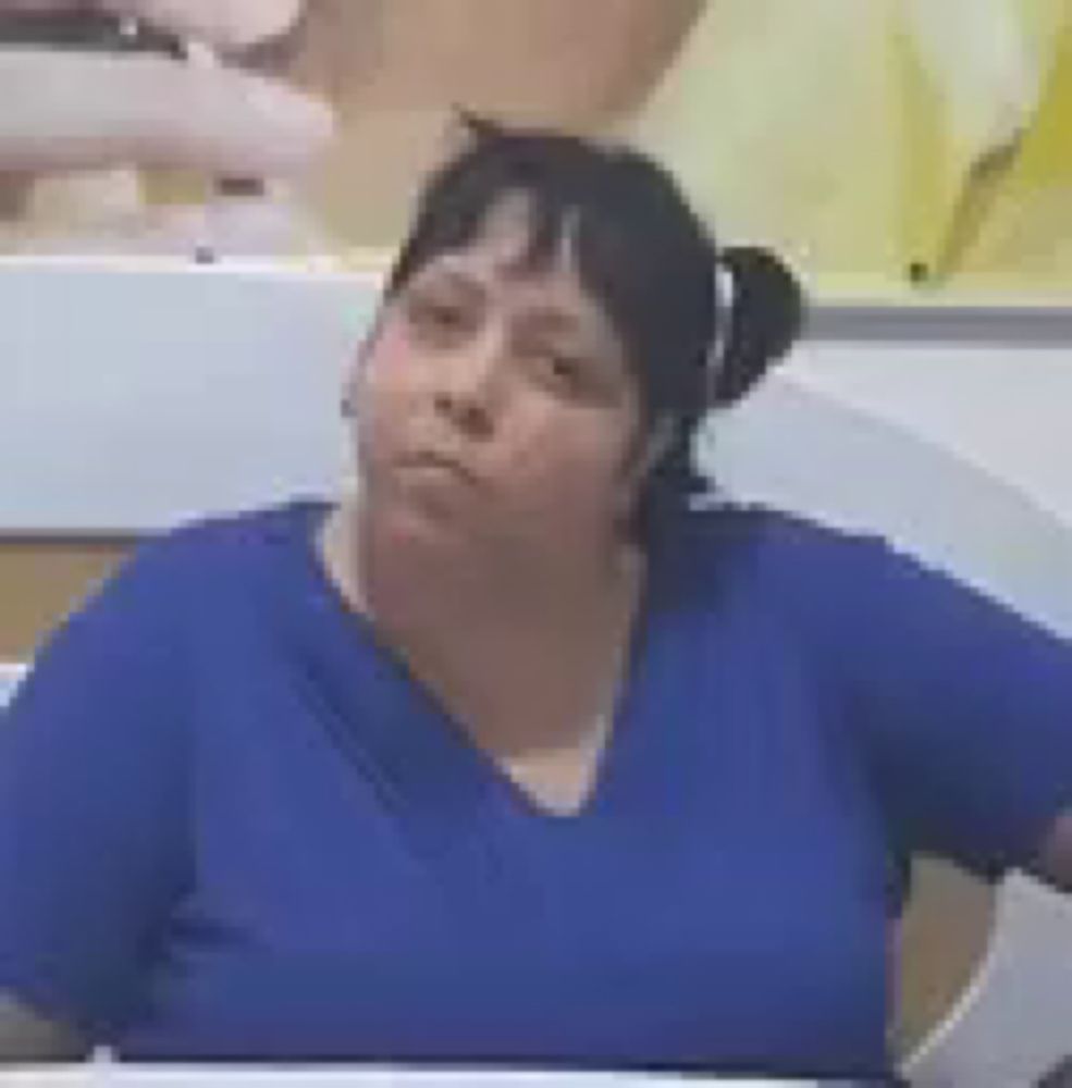 a woman in a blue scrub top is sitting at a table in front of a wall .