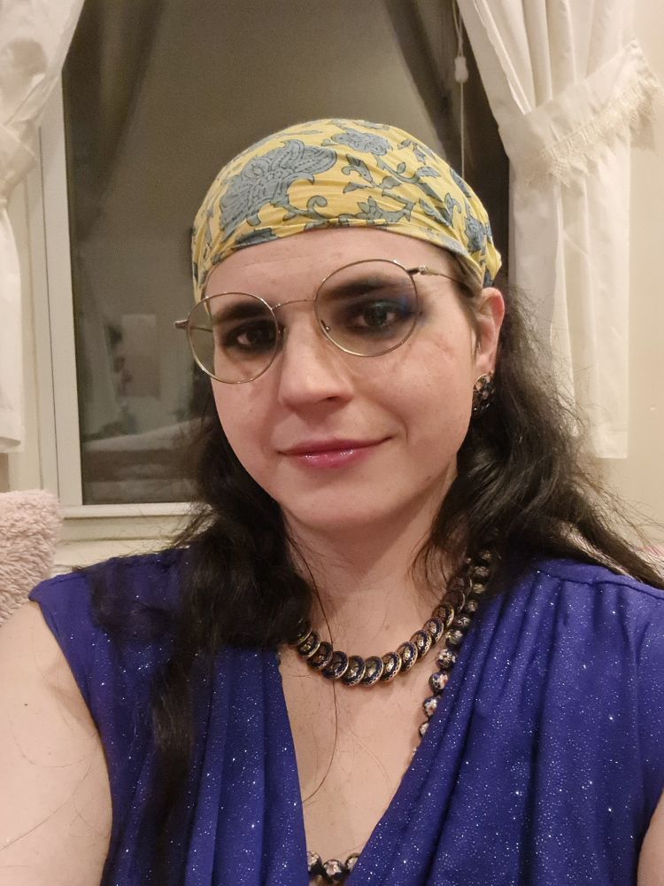 A picture of me, a white woman wearing a sparkly blue dress, with dark blue eye makeup done by my partner
