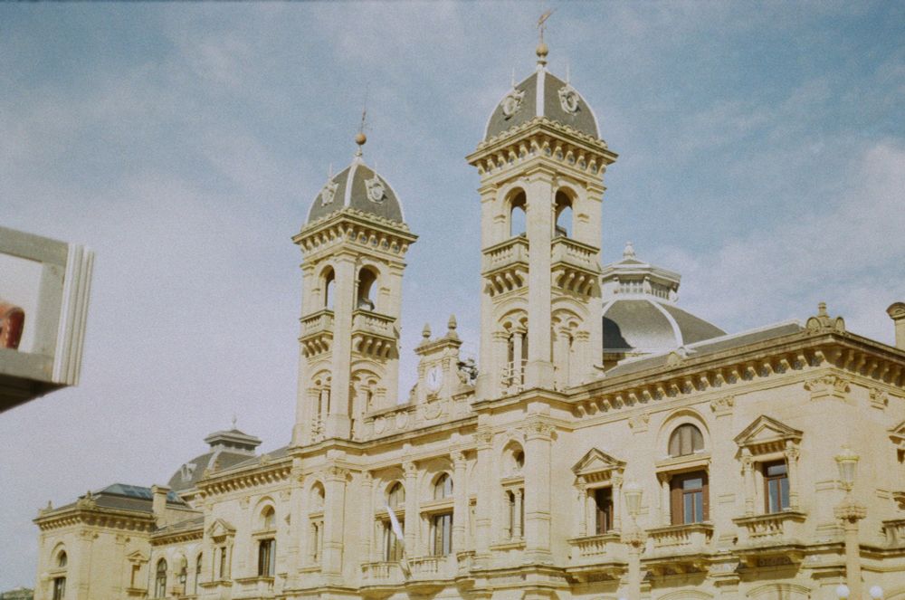 Foto d'un edifici antic, amb façana beige i dues torres de vigia. La foto ha sigut sobreexposada, donant un to de colors pastels a la llum i el cel, i un aspecte general de joguina.