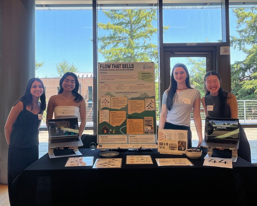Ria, Miya, Ilena, and Camryn smile next to their presentation, "Flow that Sells: Reimagining the Reuse Store at Seattle REconomy", which includes a poster, a video, a virtual tour, and other graphics. 