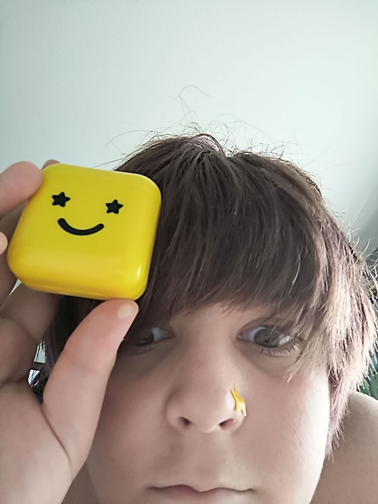 Weird woman has a star on her nose and is holding a compact mirror with a smiley face with stars for eyes printed on it
