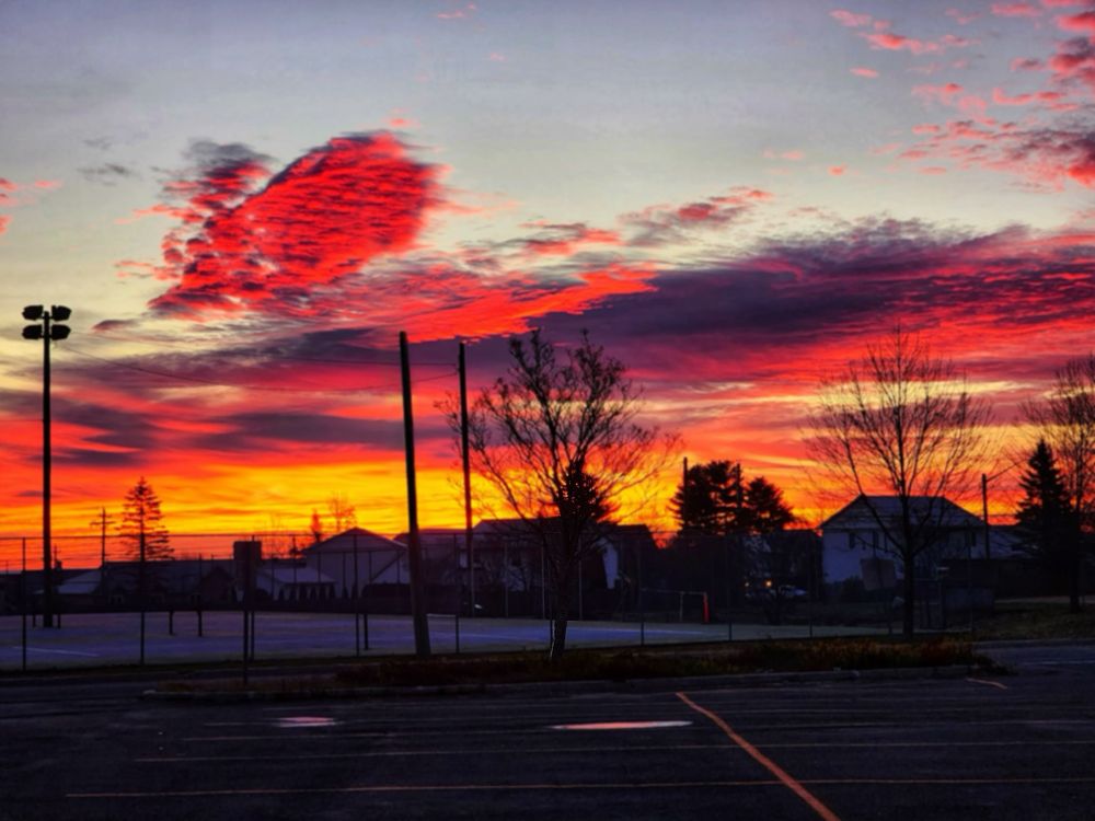 Insane sunrise at my daughter’s school, pink sporadic clouds, with dark purples, yellows. Soft blue sky in the background. Blurred houses and tennis courts in the background.