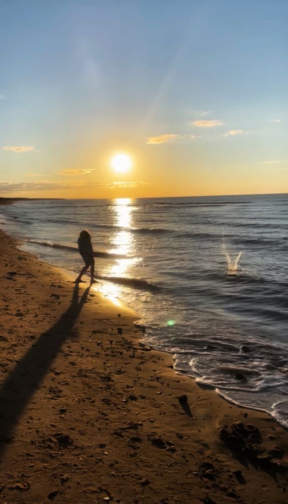My son trying his hand at skipping rocks along the ocean, in the shadow of the setting sun.