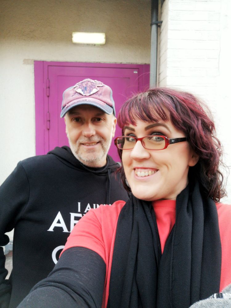 A man in a baseball cap and black hoodie and a woman with short dark hair and glasses. 