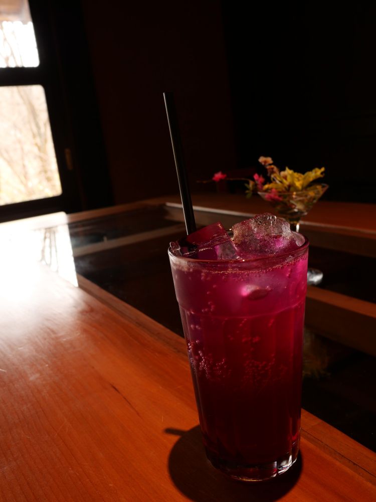 テーブルに置かれた紫蘇ジュース。背景にマティーニグラスに活けられた白梅・紅梅とトサミズキ