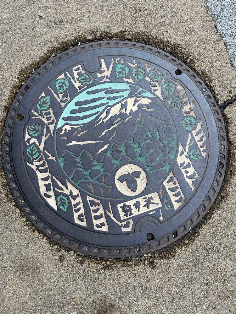 Circular manhole cover with picture of maintains and trees. 