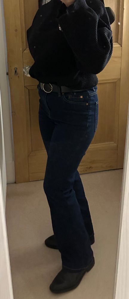 A mirror selfie of me wearing a black baggy turtleneck, boot cut jeans with a black belt and black chelsea boots.