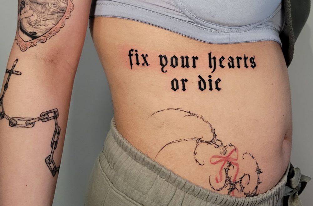 hoto of a fresh tattoo on the right side mid ribs of a person. in a gothic font called Germany the text reads, "fix your hearts or die".