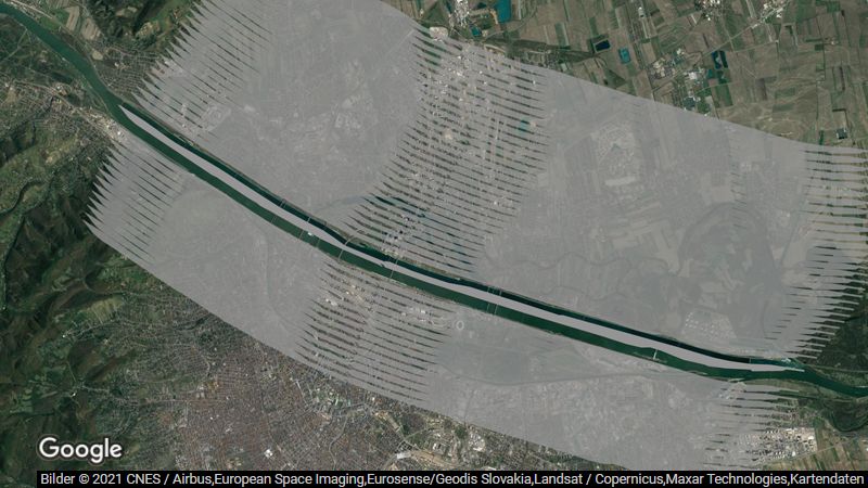 Bildbeschreibung: Luftbildaufnahme von Wien. In dem gezeigten Ausschnitt fließt die Donau von der linken oberen Bildecke Richtung rechter unterer Bildecke. Die etwas über 21 km lange Donauinsel folgt dem Verlauf der Donau. Die komplette Donauinsel ist grau eingefärbt, um die innerhalb eines Monats in Österreich versiegelte Fläche visuell darzustellen. Zusätzlich sind rechts und links davon insgesamt dreiundvierzig ebenso große Bereiche in durchsichtigem Grau eingefärbt, um die seit 1. Jänner 2022 versiegelte Fläche darzustellen.