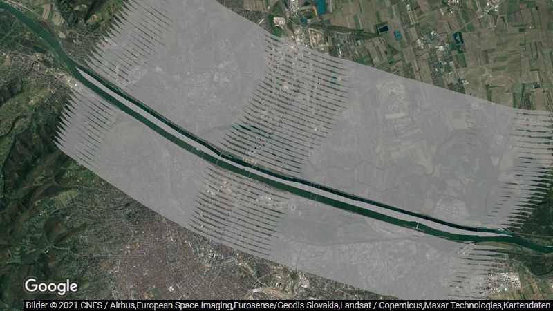 Bildbeschreibung: Luftbildaufnahme von Wien. In dem gezeigten Ausschnitt fließt die Donau von der linken oberen Bildecke Richtung rechter unterer Bildecke. Die etwas über 21 km lange Donauinsel folgt dem Verlauf der Donau. Die komplette Donauinsel ist grau eingefärbt, um die innerhalb eines Monats in Österreich versiegelte Fläche visuell darzustellen. Zusätzlich sind rechts und links davon insgesamt vierzig ebenso große Bereiche in durchsichtigem Grau eingefärbt, um die seit 1. Jänner 2022 versiegelte Fläche darzustellen.