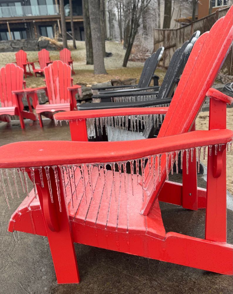 Bright red muskoka chairs on a covered in ice from ice storm. 