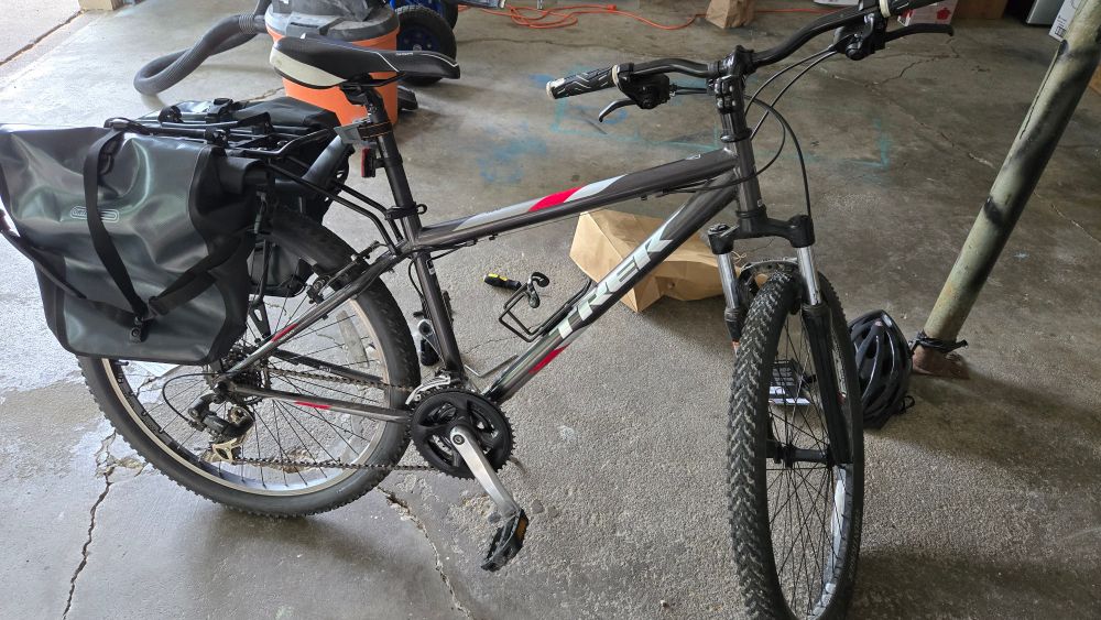 A grey, red, and white Trek branded bike with a cargo rack and saddle bags installed on it sitting in a garage