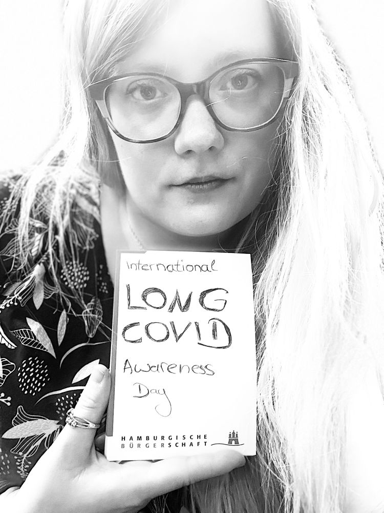 Miriam mit einem selbstgebastelten Schild auf dem international Long COVID Awareness drauf steht 