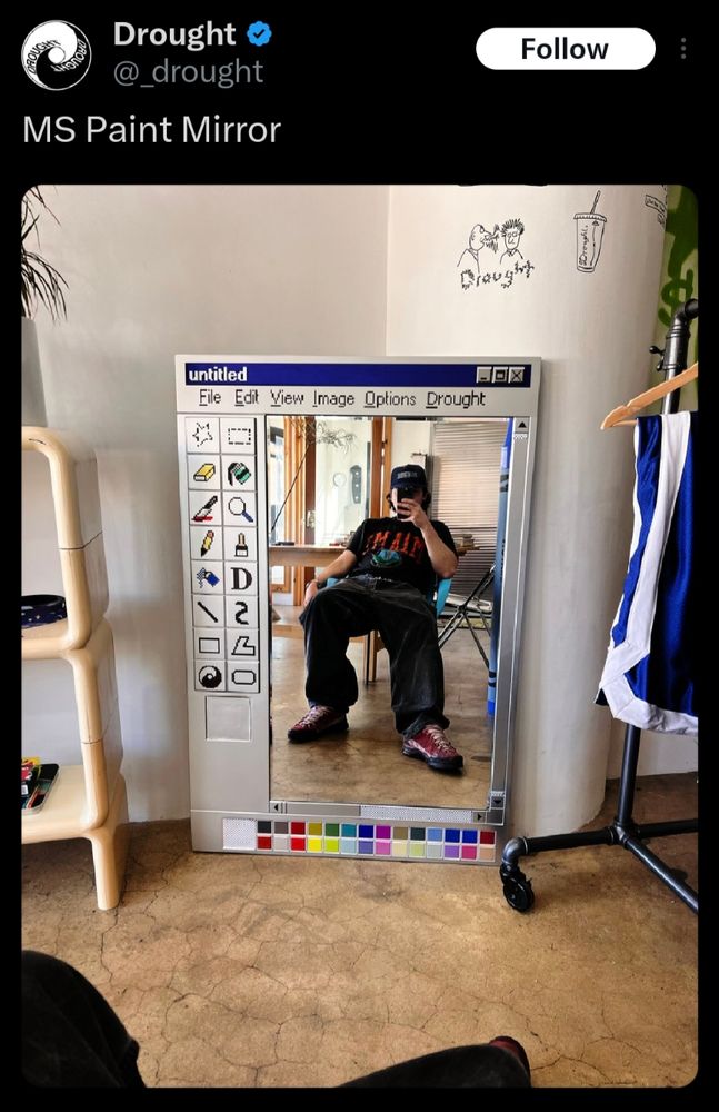 A tweet saying "MS Paint mirror". Below, a photo of a man taking a picture of himself sitting in front of a mirror. The mirror is styled to look like one of the original versions of MS Paint (the canvas which should be white is the mirror part)