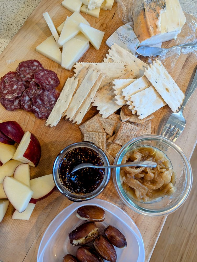 A spread of cheeses, meat, dates, caramelized onions, apple slices, crackers, and more 