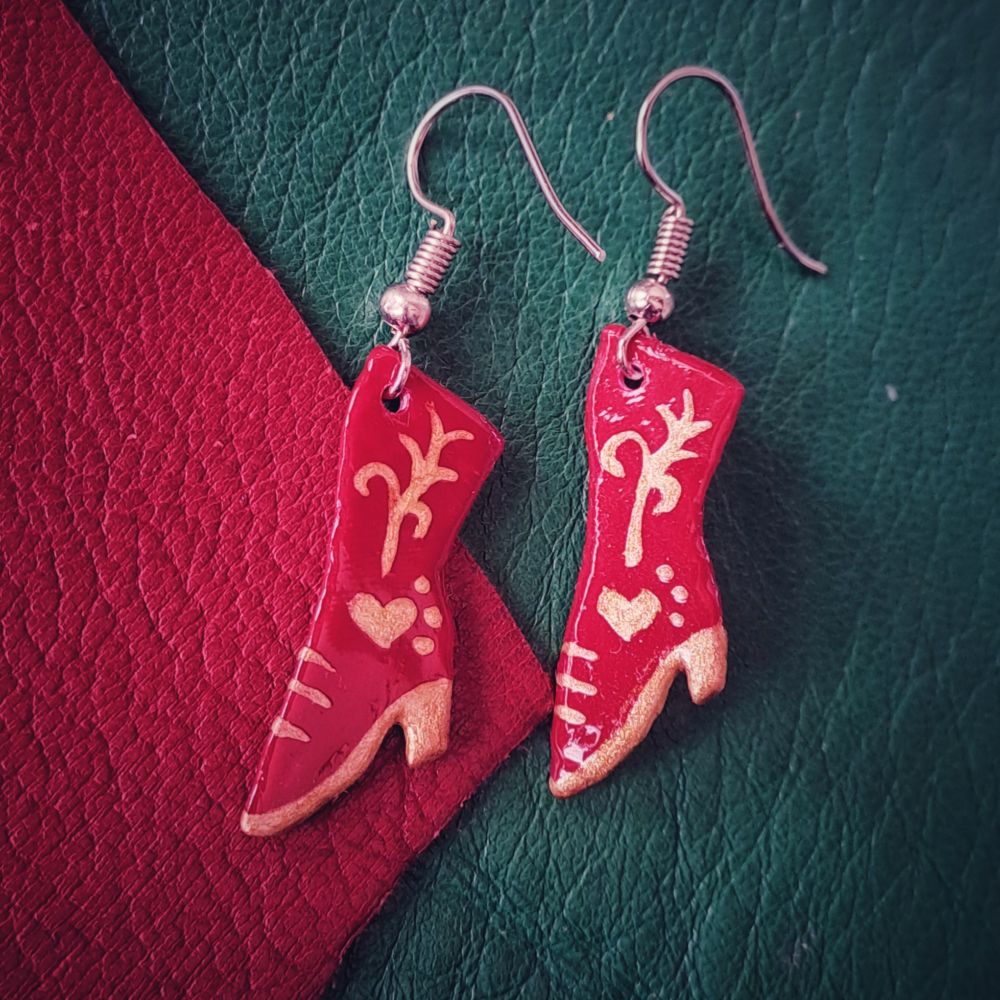Pendientes de botines rojos con detalles dorados sobre fondo verde y rojo.