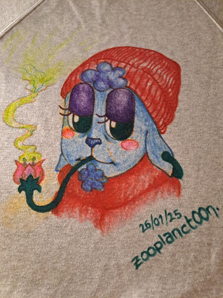 Busto de un cordero antropomorfo estilo cartoon retro con una etiqueta en la oreja, gorro y abrigo rojos y una matita de su lana en la perilla y de flequillo. Está fumando de una pipa con forma de flor. Tiene ojeras y una cicatriz en la mejilla.