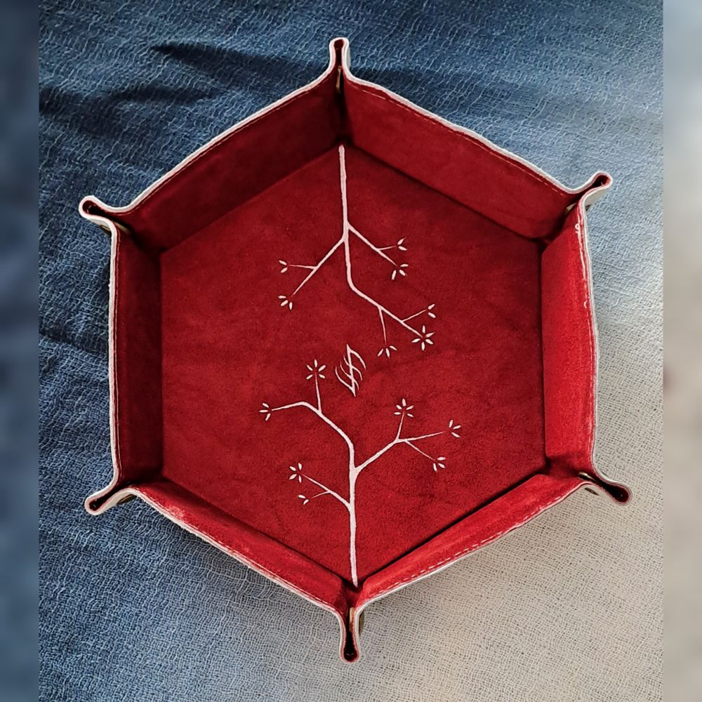 Bandeja de cuero de interior rojo con ramas blancas pintadas y un símbolo abstracto en el centro.