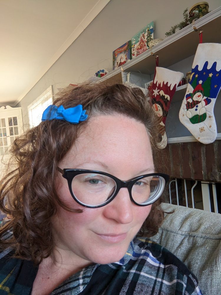 White woman with messy curly hair all swept over to one side and secured with a blue grosgrain toddler ribbon