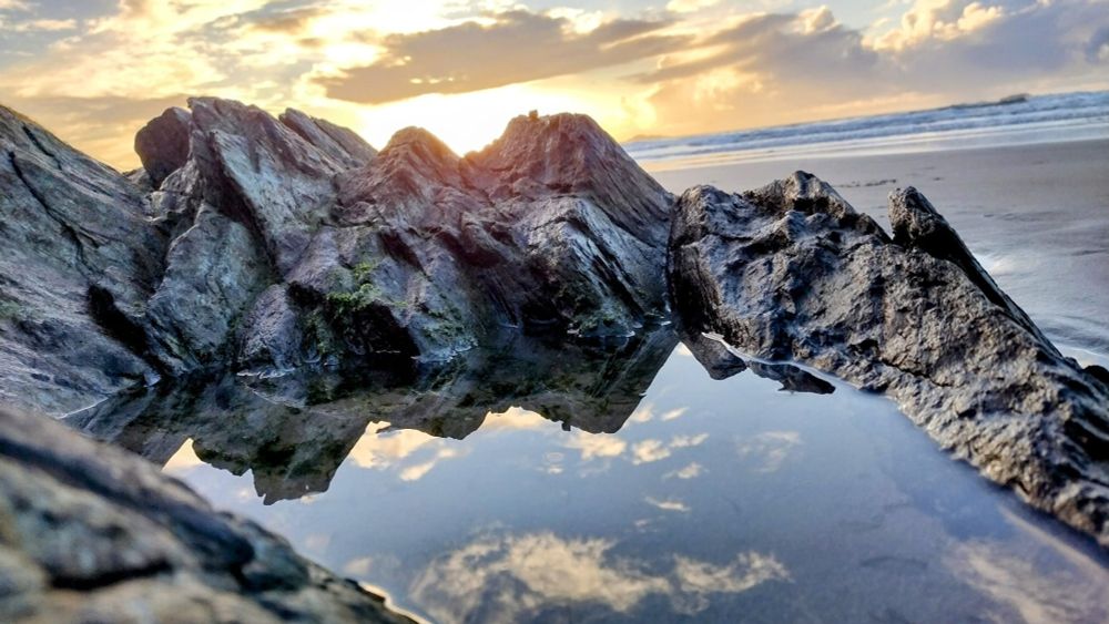 A rockpool in South Wales with sand and autumnal sunset, the sky reflected in the pool.
