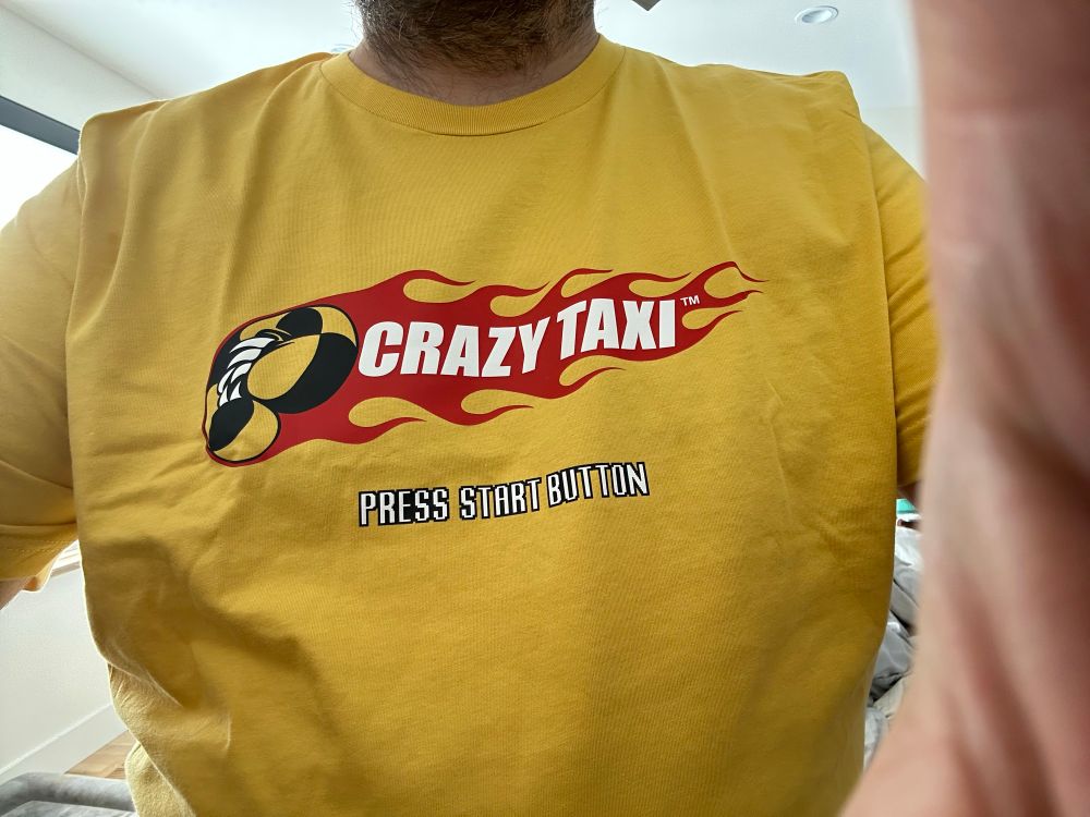 a yellow tshirt with the Crazy Taxi logo that says “PRESS START BUTTON”