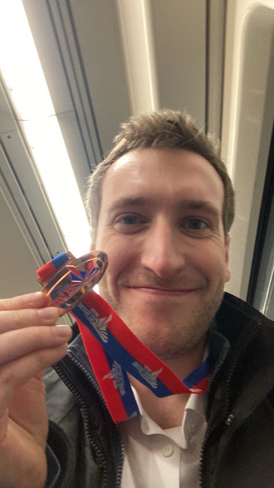 Keenan smiling on a Sheffield tram holding a bronze medal that says ‘British Ice Skating’ on it