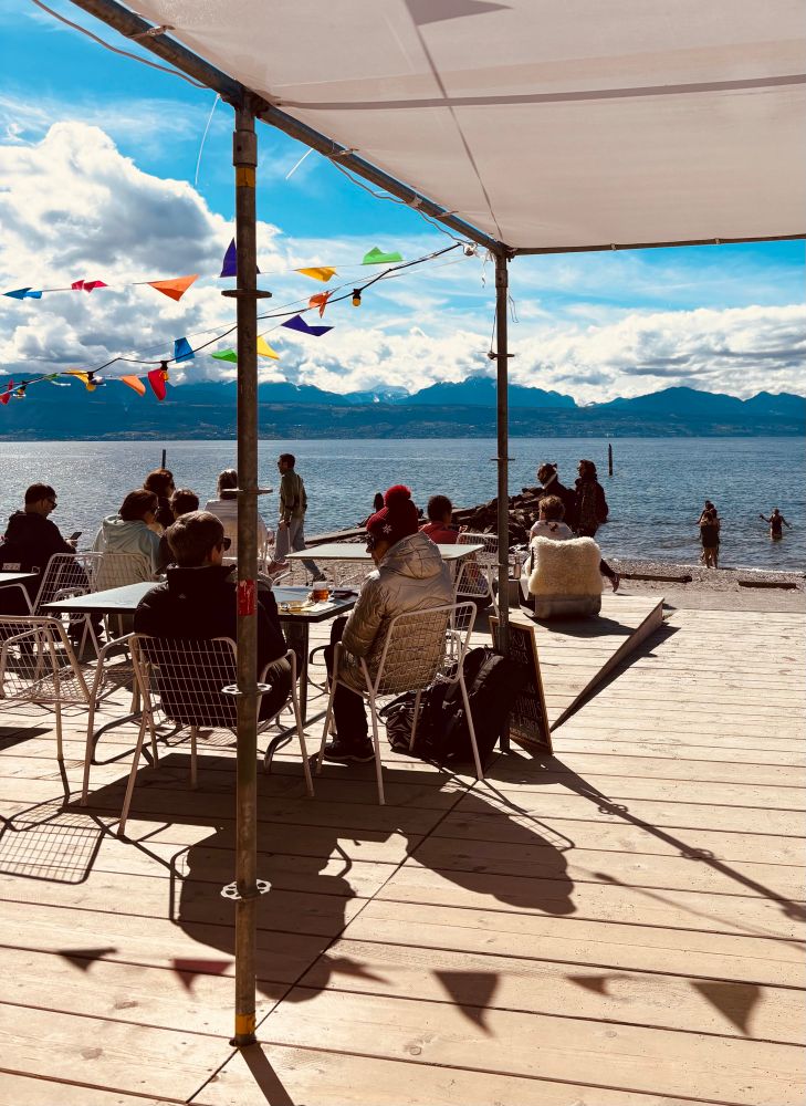 View of the leman lake beach on a sunny Sunday morning from the Bain’s des Rives sauna. People are bathing.