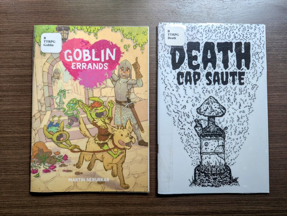 Two TTRPGs laying on a table, side by side, front cover up. Goblin Errands and Death Cap Saute.