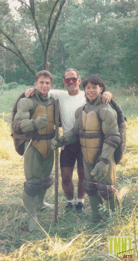 a behind-the scenes photo from Teenage Mutant Ninja Turtles (1990) featuring three people, two of them in the martial arts stunt TMNT suits but without the heads. I recognize the one on the right as Ernie Reyes Jr., who went on to play Keno in TMNT II: Secret of the Ooze