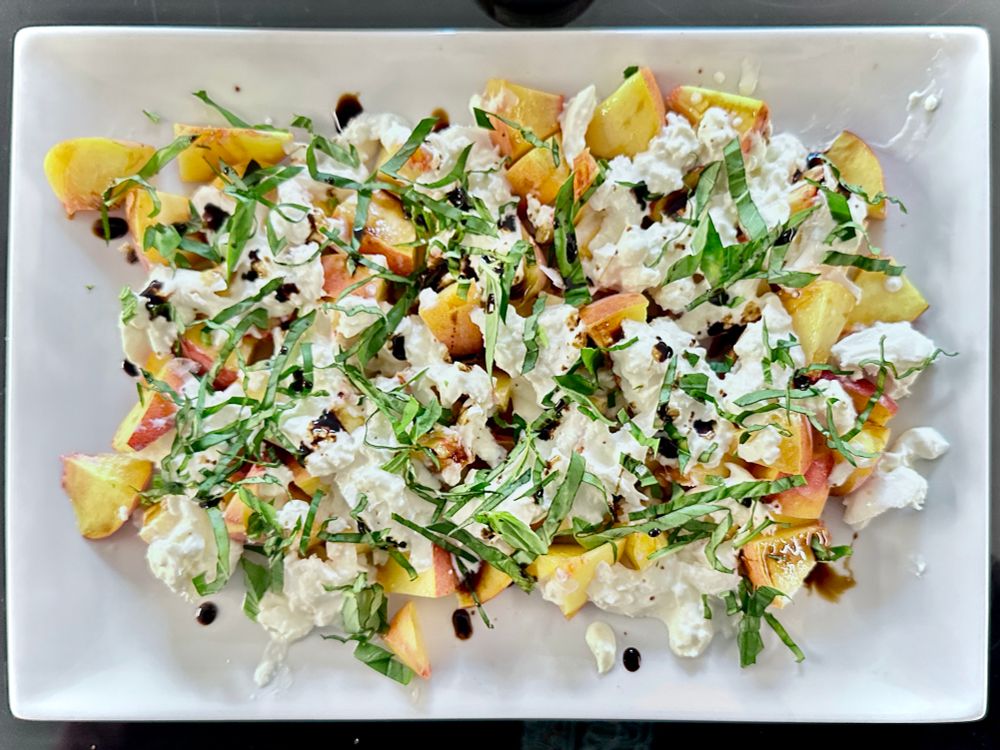 top down view of peaches, burrata, basil, and balsamic vinegar mixed on a platter