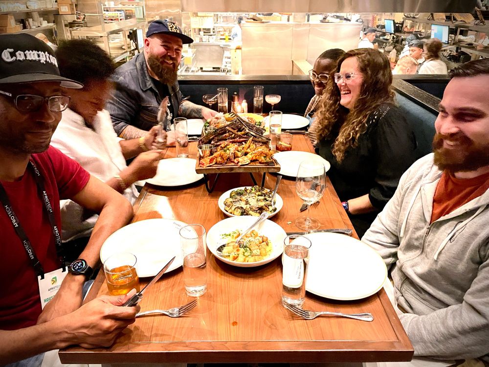 the group at the Guard + Grace with a feast on the table. everyone is laughing except Anthony, who’s mugging for the camera