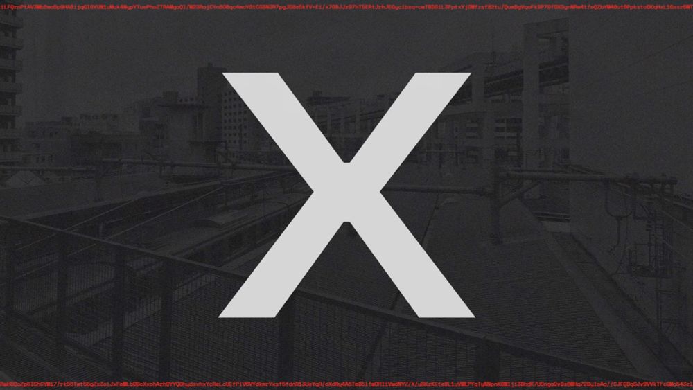 A video still from the video for 'c0n73x7_c0ll4p53'.  The background is a dark grey photograph looking out over a train yard in Chiba. On the top and bottom edge is small red text that is just strings of characters, its encrypted text. In the venter is a massive white X. 