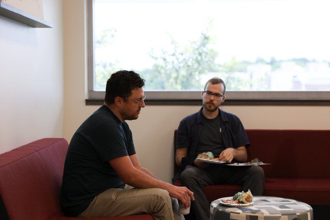 Adam Ghazi-Tehrani sits on a couch in the foreground with Ben Battafarano sitting on an adjacent couch looking at him.