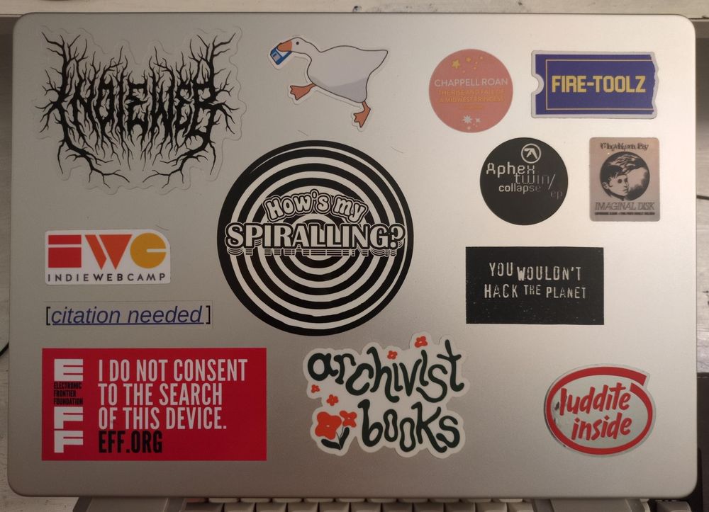 A silver laptop covered in stickers. At the bottom right is a new one that reads "Luddite inside" imitating the “Intel inside” design. The foreground is in red and the background is silver.