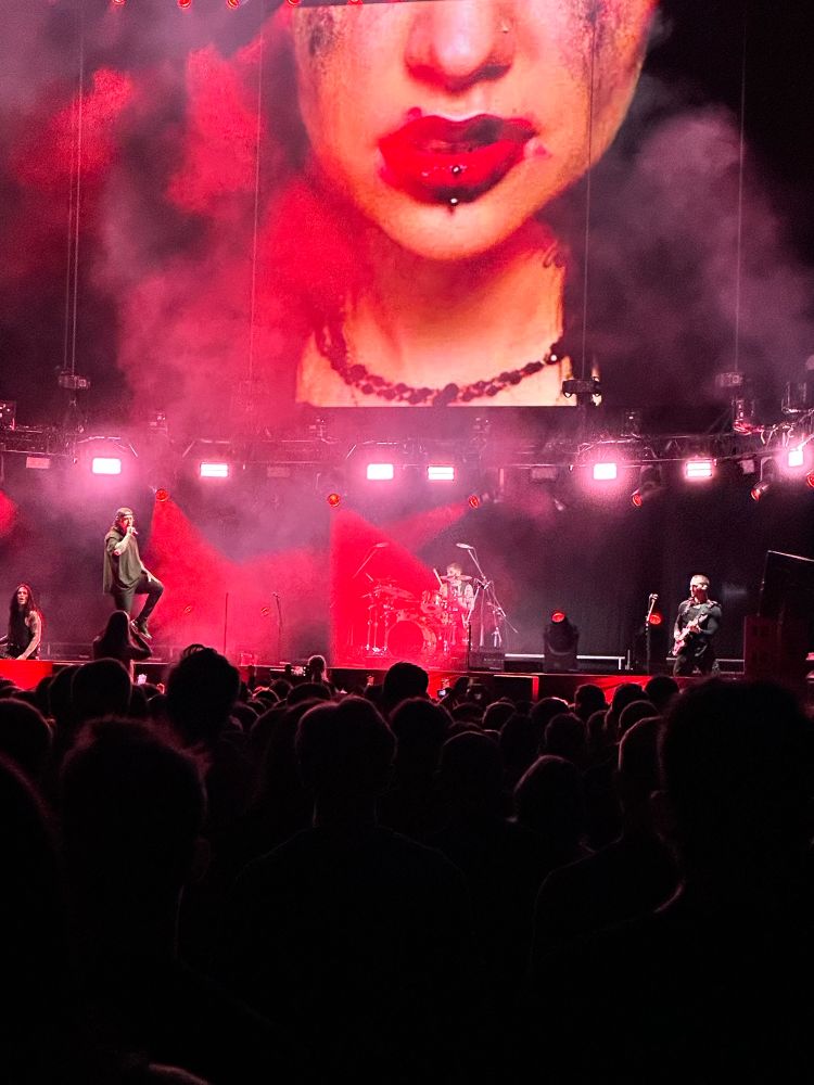 falling in reverse concert, red lights and smoke on stage. screen displays woman with messy makeup for the song ‘situations’