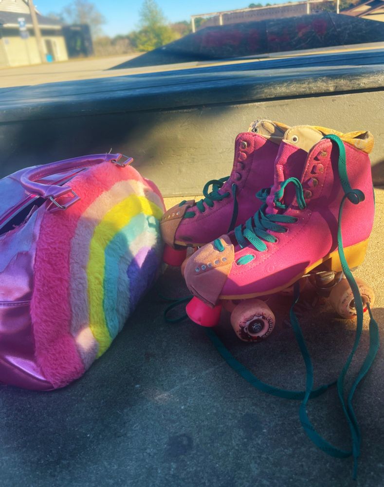 Rachael’s pink roller skates and pink and rainbow skate park sitting on the ground at the skate park