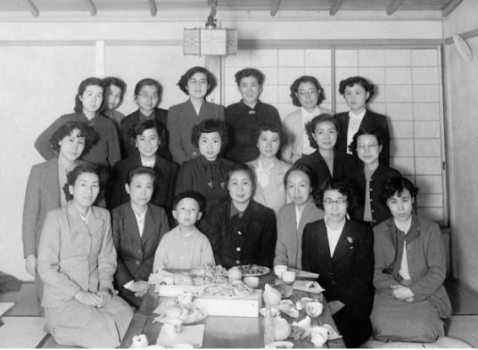 A photo of a group of women (and one child) celebrating at a traditional Japanese meal. Katō is seated in the center at the front of the group.