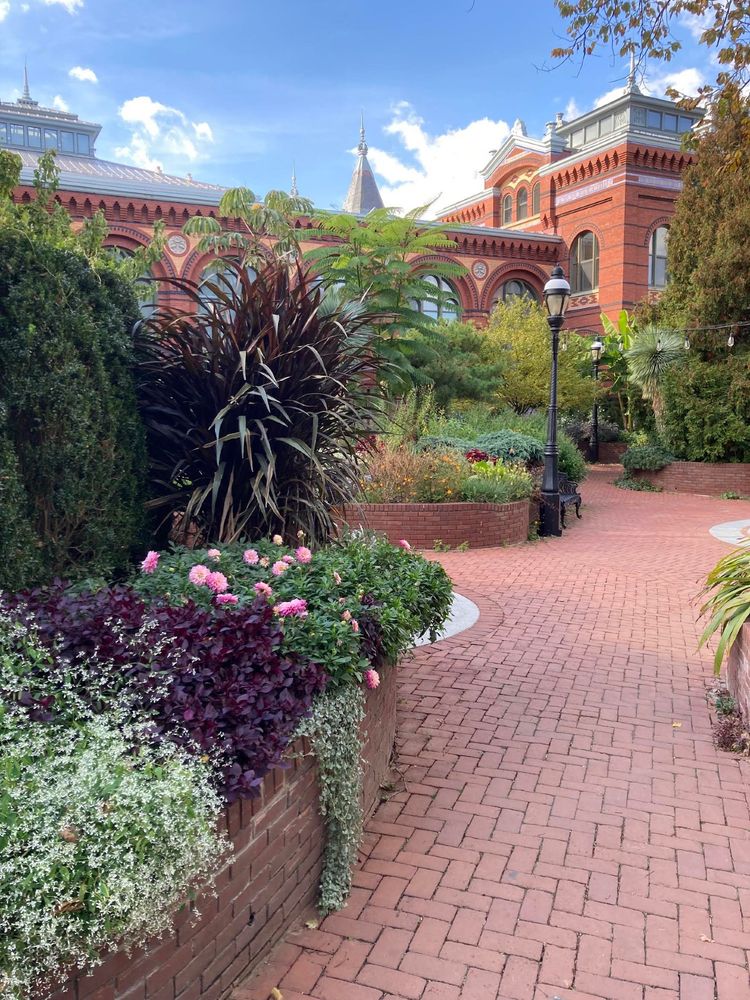 A brick path filled with flowering plants and the Smithsonian Museum in the background.