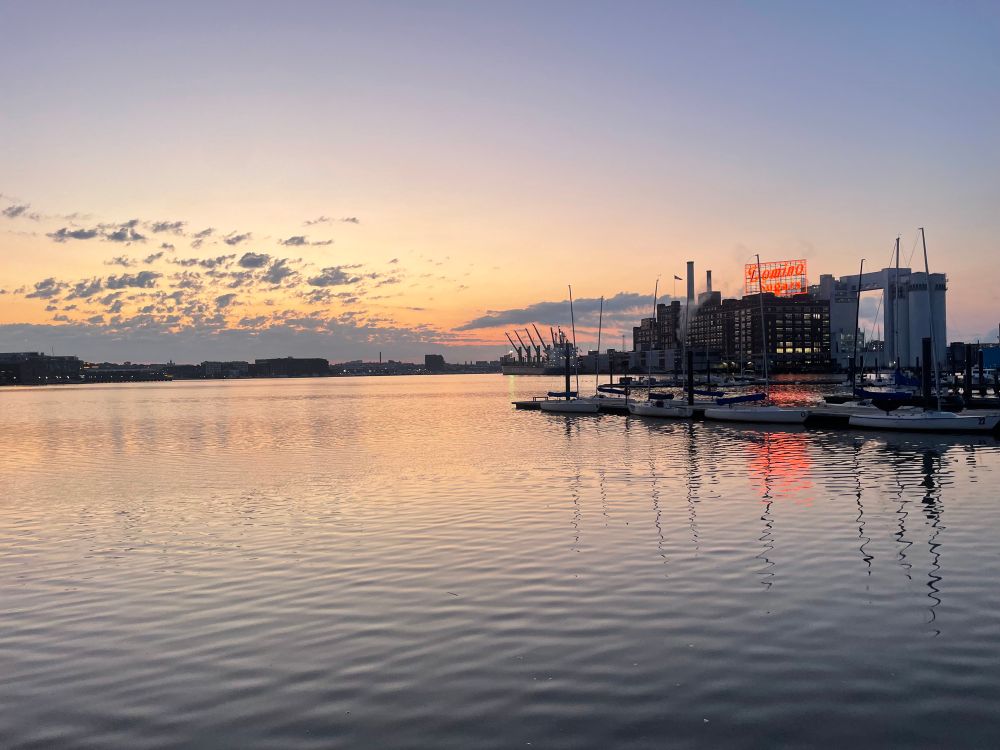 Sunrise over a harbor/marina, with a few clouds, the Domino Sugar plan in the background.