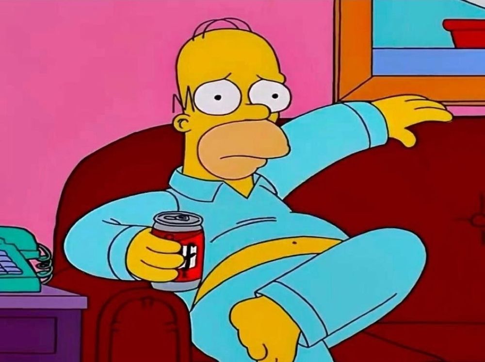 Homer simpson is trying to chill on the couch but has a frown on his face and anxiety.
