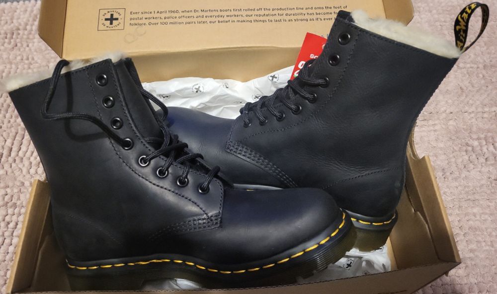 A pair of black doc marten boots in a shoe box. The shoes are different sizes.