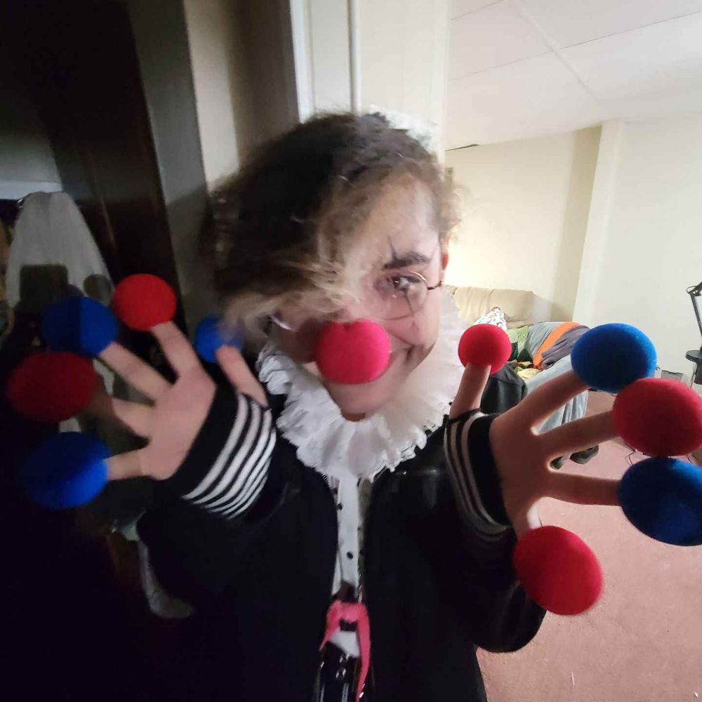 its genderbug! shes dressed luke a clown, with a white frill, red nose and eye makeup. shes got a clown nose on each of her fingers, alternating red and blue. her worm joel can be seen hanging from her neck.